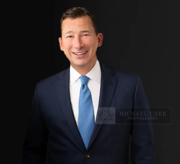 Professional Houston Business Headshots of a man in a navy suit and blue tie against a black background.