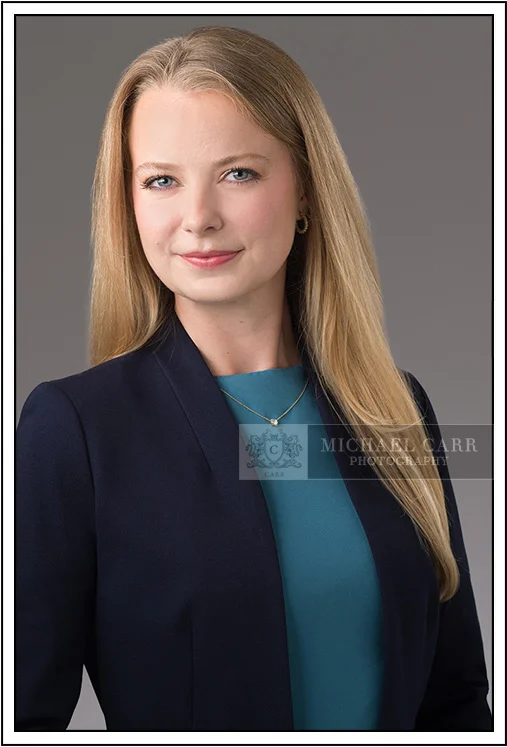 Houston Headshot Photographer Professional classic business headshot of a woman wearing a navy blazer and teal blouse on a gray studio background in Houston, Texas.