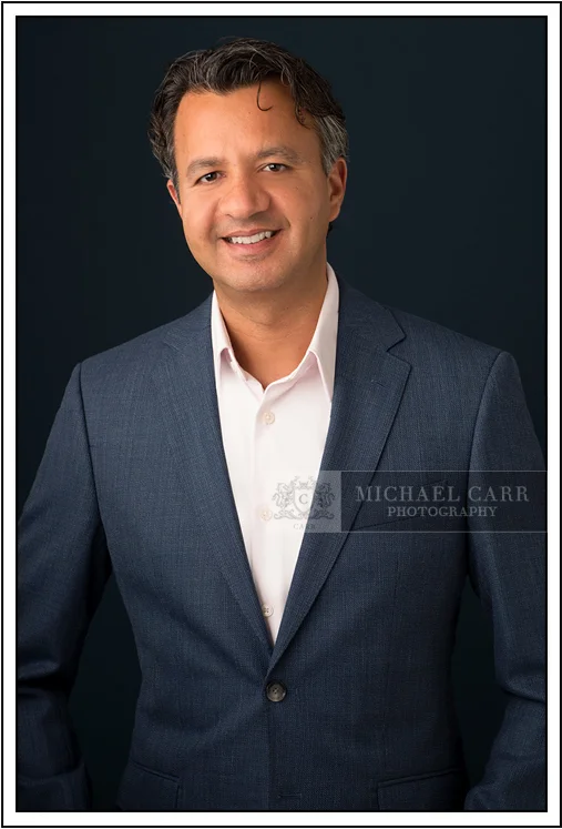 Houston Headshot Photographer Professional Houston corporate headshot of a business executive wearing a blue suit against a dark studio background.