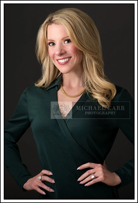 Houston Headshot Photographer Professional headshot of a woman C-suite executive wearing a green dress against a dark gray studio background.